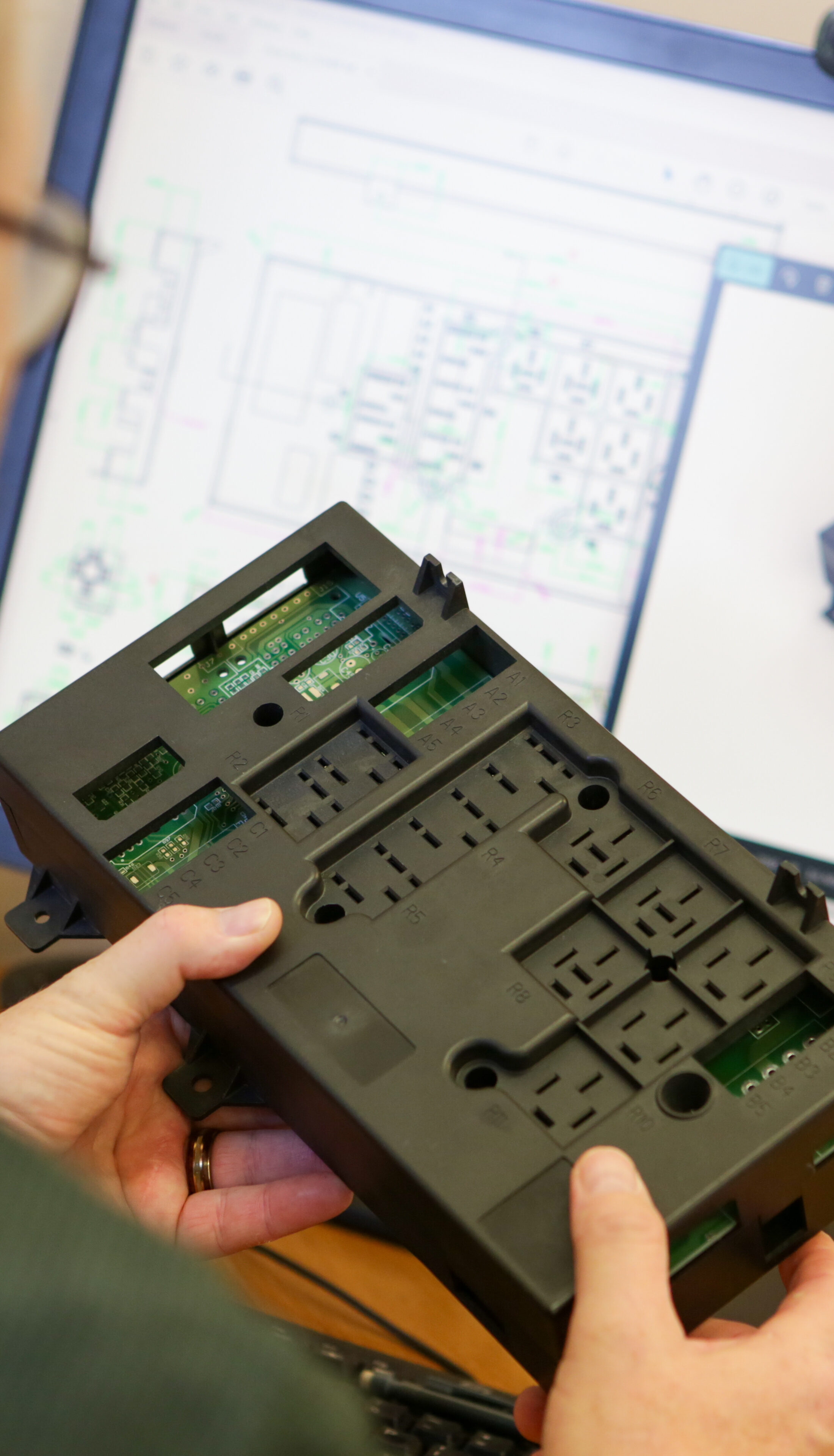 An engineer holding a product with the CAD drawing of it on a screen in front of him.